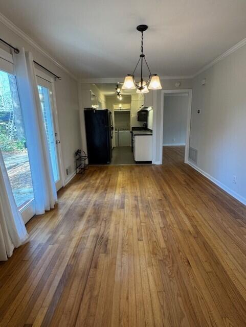 unfurnished dining area with light wood-style floors, visible vents, crown molding, and baseboards