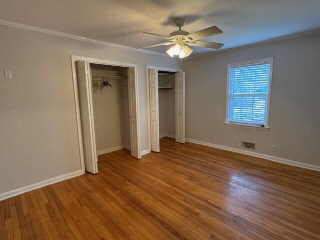 unfurnished bedroom featuring crown molding, baseboards, multiple closets, and wood finished floors