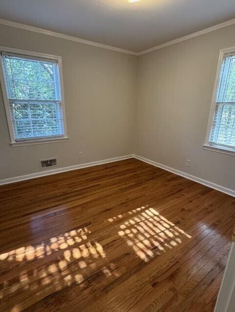 unfurnished room with dark wood-style floors, ornamental molding, visible vents, and baseboards