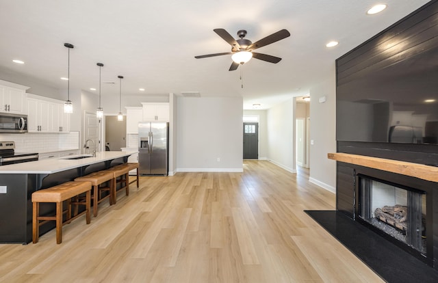 kitchen with a breakfast bar area, light wood-style flooring, a fireplace with raised hearth, stainless steel appliances, and white cabinets