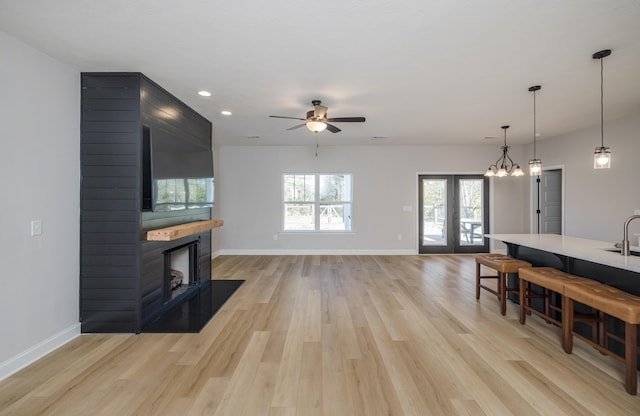 living room featuring baseboards, a large fireplace, light wood-style flooring, and french doors