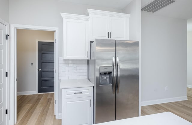 kitchen featuring visible vents, light countertops, light wood-style floors, stainless steel refrigerator with ice dispenser, and tasteful backsplash