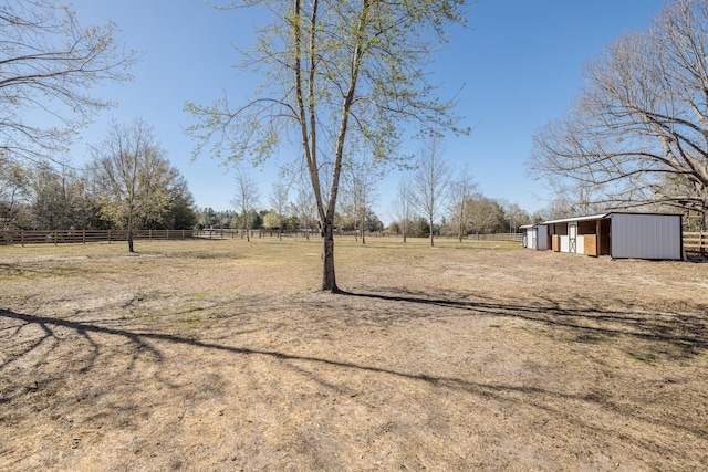 view of yard with a rural view, an outdoor structure, fence, and an outbuilding