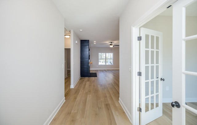 hall with light wood-style floors, baseboards, and french doors