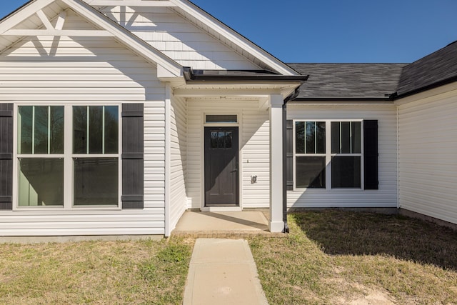 view of exterior entry featuring a lawn and roof with shingles