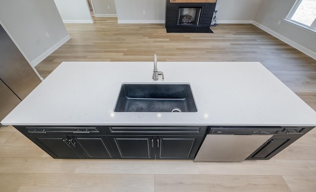 kitchen with baseboards, a fireplace with flush hearth, a sink, stainless steel dishwasher, and dark cabinets