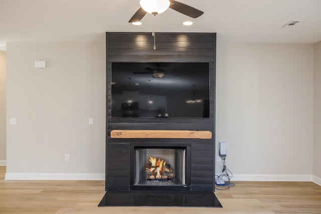 details with visible vents, a large fireplace, baseboards, ceiling fan, and wood finished floors