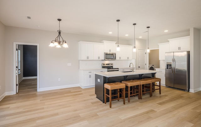 kitchen featuring white cabinetry, a sink, stainless steel appliances, a kitchen bar, and backsplash