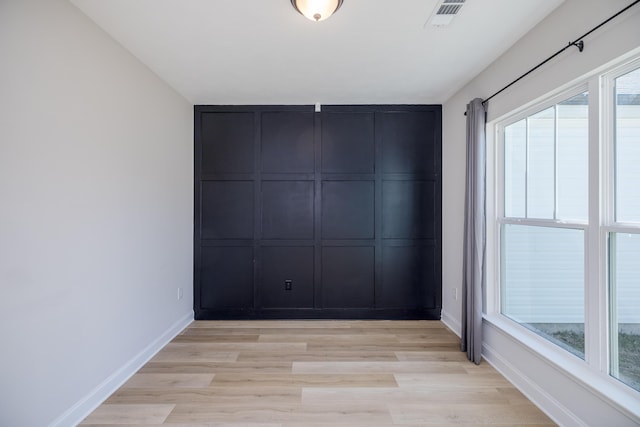 unfurnished room featuring light wood-style floors, a healthy amount of sunlight, visible vents, and baseboards