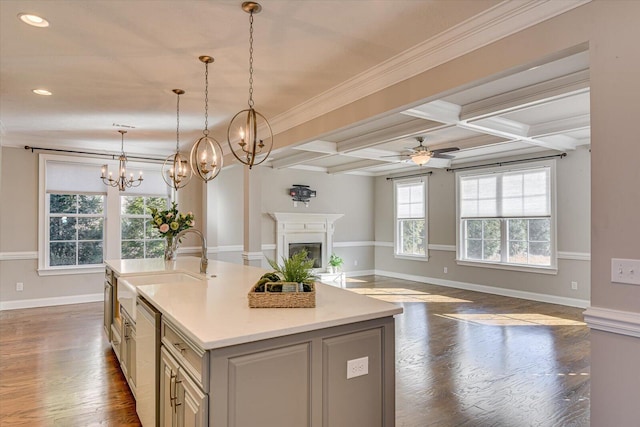 kitchen with dark wood-type flooring, coffered ceiling, hanging light fixtures, a center island with sink, and beamed ceiling