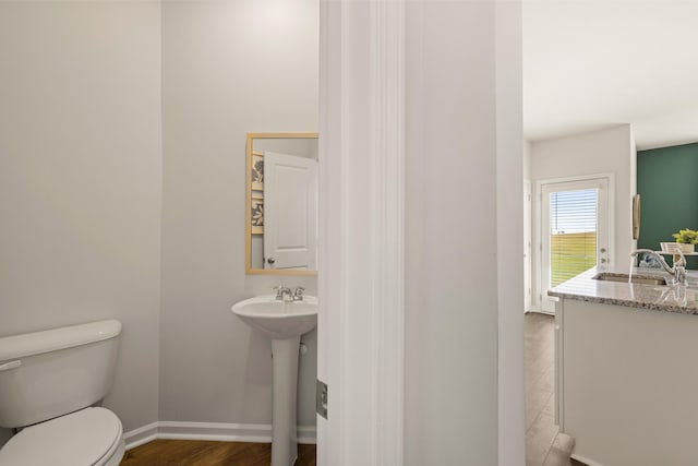 half bathroom featuring wood finished floors, baseboards, a sink, and toilet