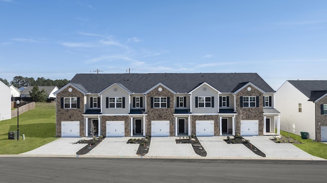 townhome / multi-family property with stone siding, fence, a front yard, and concrete driveway