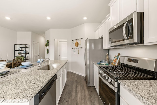 kitchen with white cabinets, a sink, light stone countertops, appliances with stainless steel finishes, and dark wood-style flooring