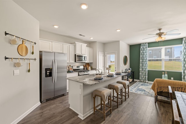 kitchen featuring a breakfast bar area, stainless steel appliances, a center island with sink, white cabinets, and visible vents