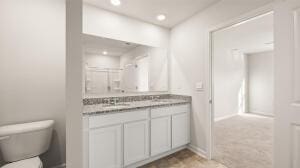 full bath featuring toilet, a sink, double vanity, and recessed lighting