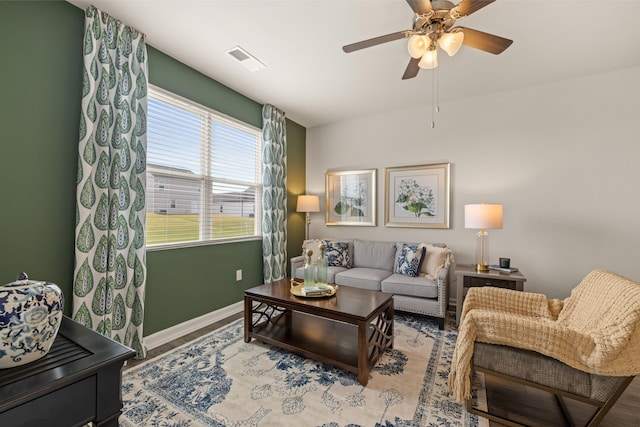 living area featuring wood finished floors, visible vents, baseboards, and ceiling fan