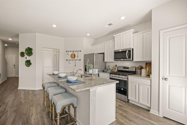 kitchen with appliances with stainless steel finishes, a sink, a kitchen island with sink, and light wood-type flooring