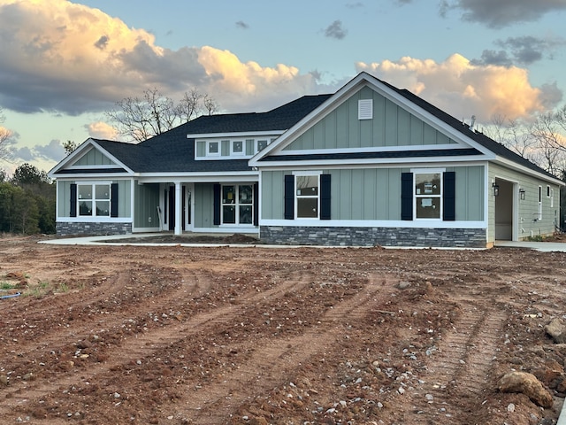 view of front facade featuring stone siding, a shingled roof, and board and batten siding