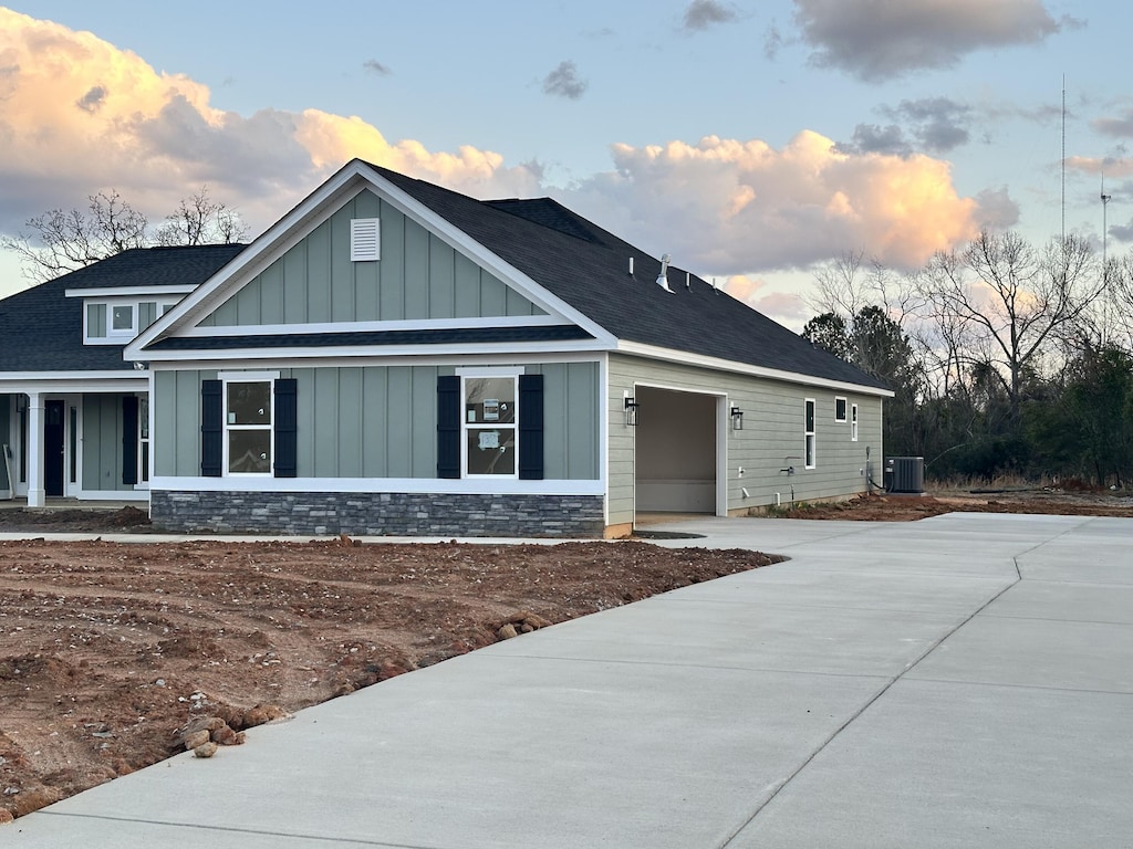 view of front of house featuring concrete driveway, an attached garage, board and batten siding, cooling unit, and stone siding