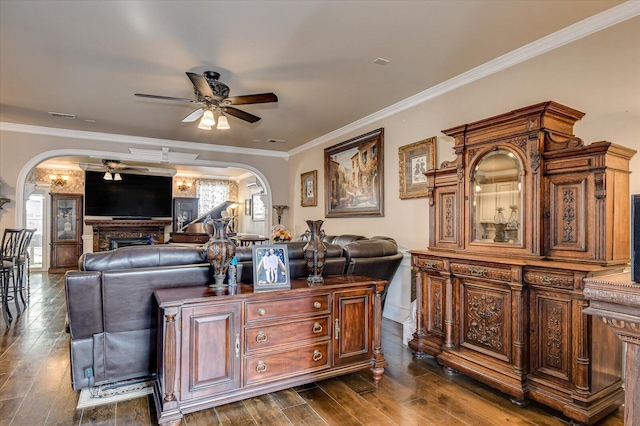 living room featuring ceiling fan, a fireplace, dark hardwood / wood-style floors, and ornamental molding