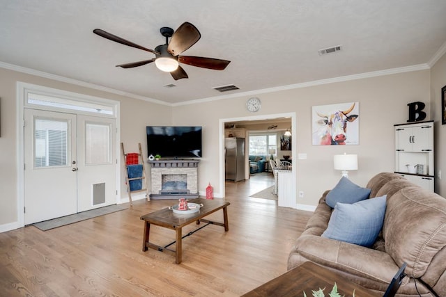 living room featuring ceiling fan, ornamental molding, a fireplace, and light hardwood / wood-style floors