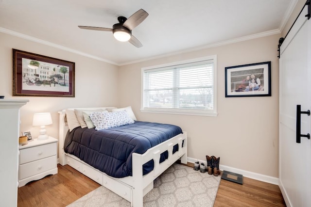 bedroom with ornamental molding, a barn door, ceiling fan, and light hardwood / wood-style floors