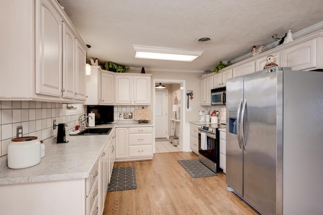 kitchen with sink, white cabinetry, light hardwood / wood-style flooring, appliances with stainless steel finishes, and decorative backsplash