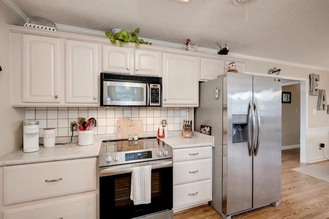 kitchen with decorative backsplash, ornamental molding, stainless steel appliances, and light wood-type flooring