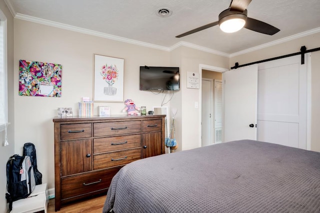 bedroom with ceiling fan, ornamental molding, a barn door, and light hardwood / wood-style floors