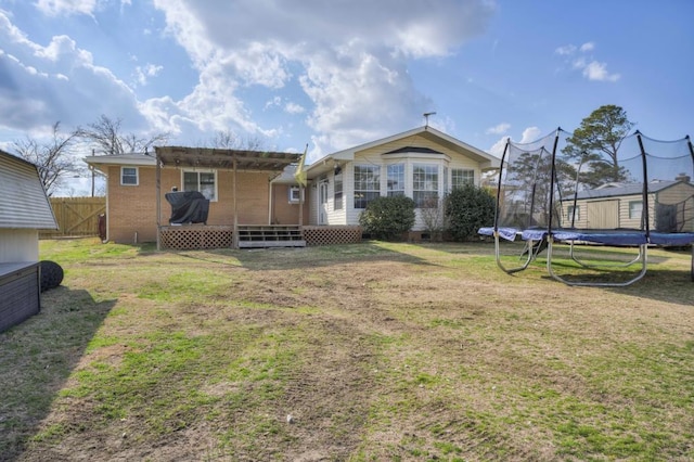 rear view of house featuring a trampoline and a lawn