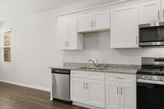 kitchen with light stone countertops, appliances with stainless steel finishes, dark hardwood / wood-style flooring, sink, and white cabinets