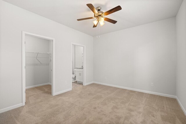 unfurnished bedroom featuring ceiling fan, a walk in closet, light carpet, and ensuite bath