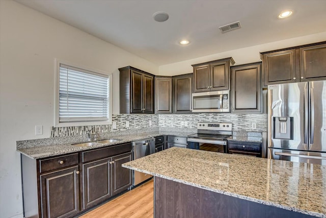 kitchen featuring dark brown cabinetry, sink, light stone counters, light hardwood / wood-style floors, and appliances with stainless steel finishes