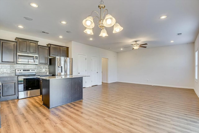 kitchen with decorative backsplash, appliances with stainless steel finishes, ceiling fan with notable chandelier, pendant lighting, and a kitchen island