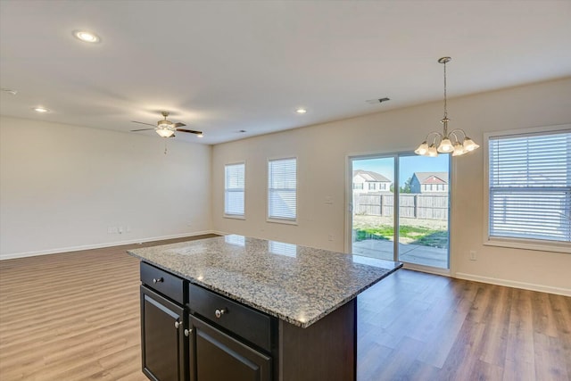 kitchen with a wealth of natural light, ceiling fan with notable chandelier, hardwood / wood-style flooring, a kitchen island, and hanging light fixtures