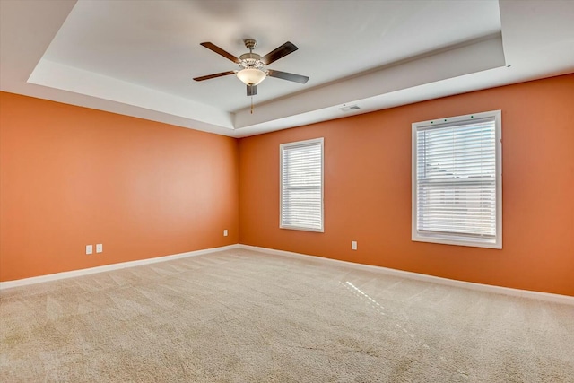 carpeted empty room with ceiling fan and a raised ceiling