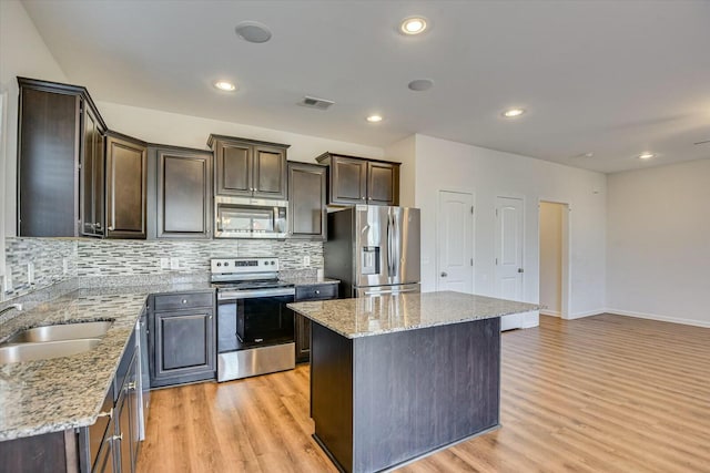 kitchen featuring sink, a kitchen island, light stone counters, and stainless steel appliances