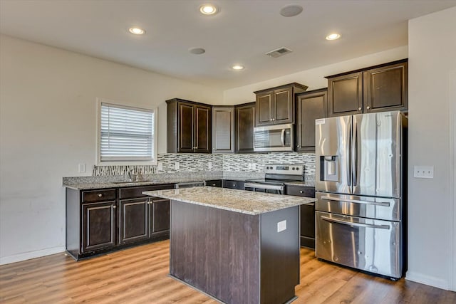 kitchen with light hardwood / wood-style flooring, light stone countertops, dark brown cabinets, a kitchen island, and stainless steel appliances