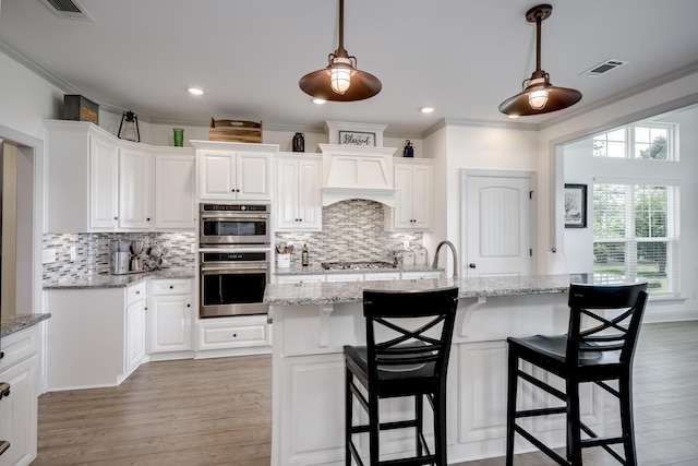 210 Rivernorth Dr, North Augusta, SC 29841 - kitchen featuring stainless steel appliances, premium range hood, light wood finished floors, white cabinetry, and ornamental molding
