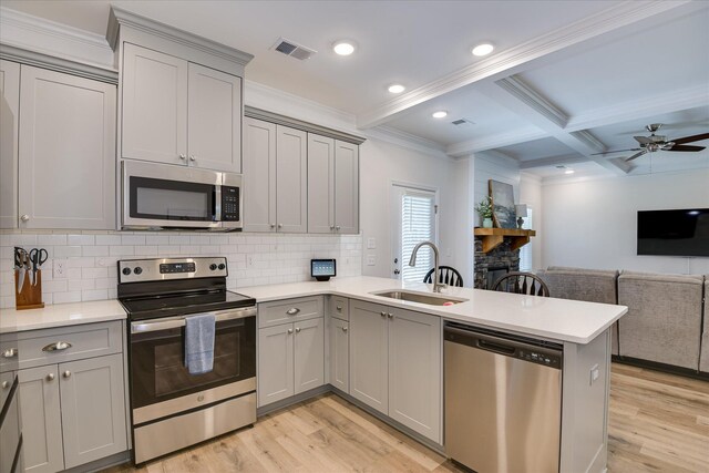 kitchen featuring a peninsula, gray cabinets, a sink, light wood-style flooring, and appliances with stainless steel finishes