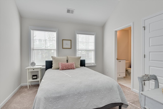 bedroom featuring light colored carpet, visible vents, vaulted ceiling, baseboards, and ensuite bath