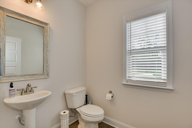 half bath with toilet, baseboards, and a sink
