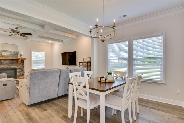 dining space featuring a stone fireplace, crown molding, beamed ceiling, ceiling fan with notable chandelier, and light wood-style floors