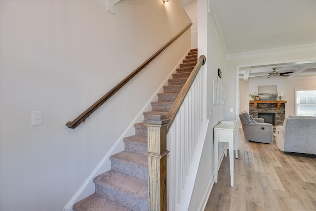 staircase with ornamental molding, beam ceiling, wood finished floors, a fireplace, and a ceiling fan