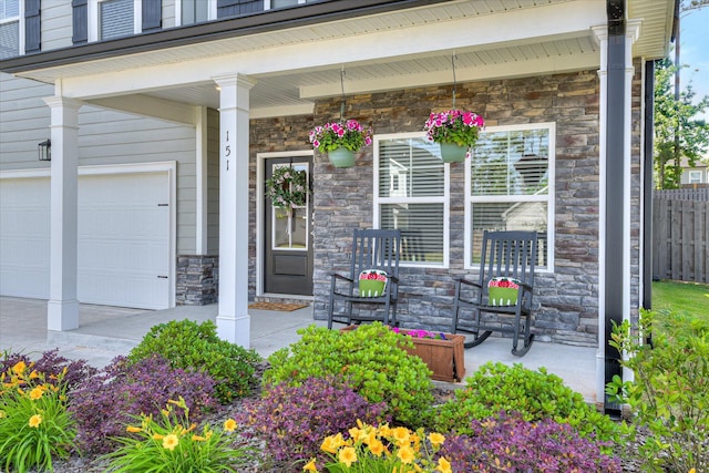 view of exterior entry featuring an attached garage, fence, covered porch, and stone siding
