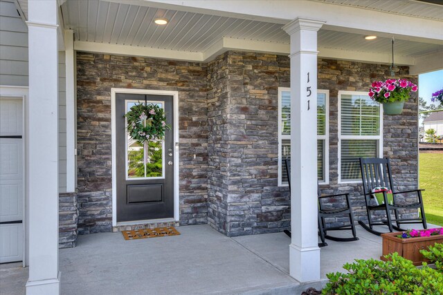 view of exterior entry featuring covered porch and stone siding