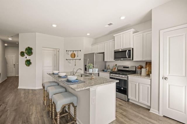 kitchen featuring white cabinetry, stainless steel appliances, an island with sink, sink, and a kitchen breakfast bar