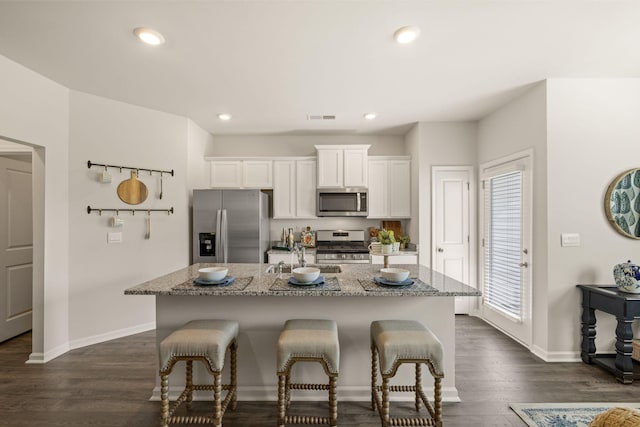 kitchen featuring white cabinets, a kitchen bar, appliances with stainless steel finishes, and an island with sink