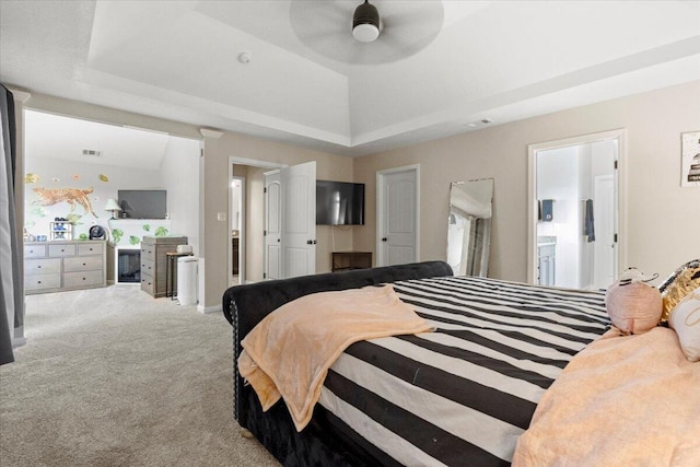 carpeted bedroom featuring a tray ceiling, ceiling fan, and ensuite bathroom