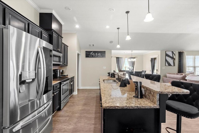 kitchen featuring a large island with sink, a kitchen breakfast bar, sink, hanging light fixtures, and appliances with stainless steel finishes